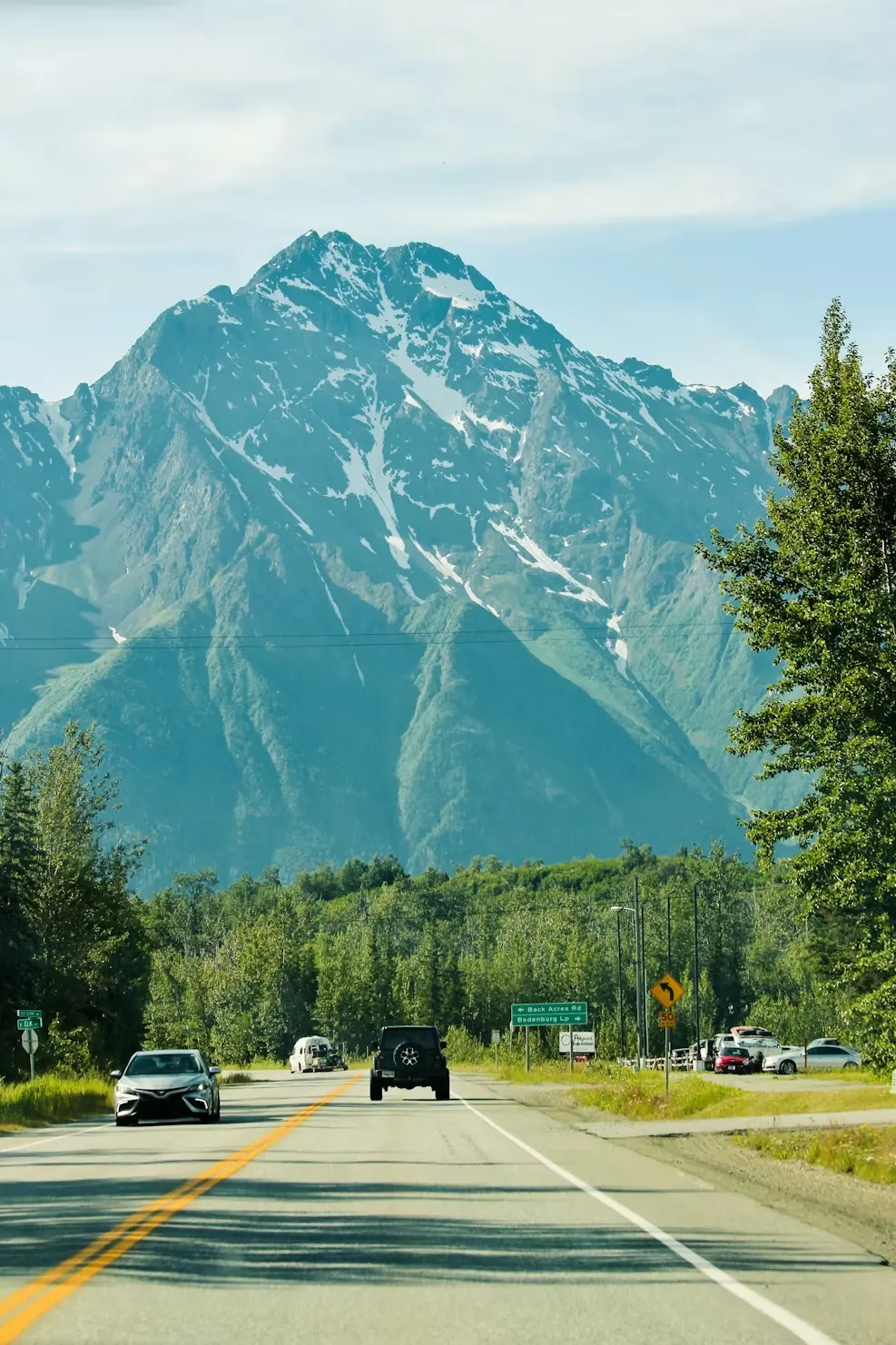 A highway leading toward a snow-capped Alaska mountain