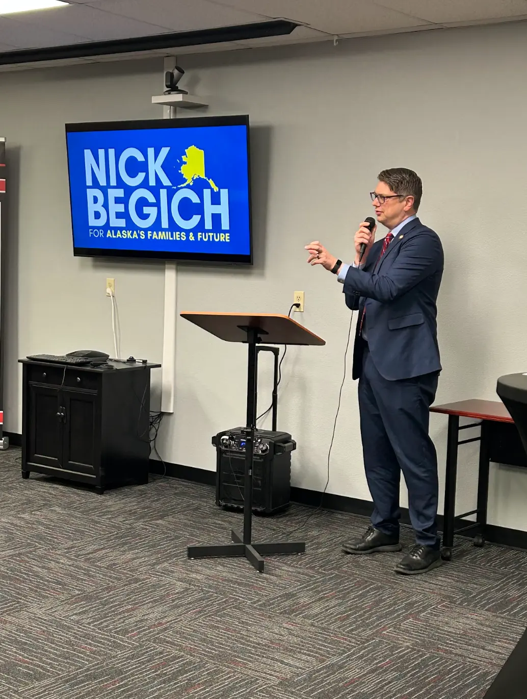 Congressman Begich speaking at a town hall in front of a Nick Begich sign